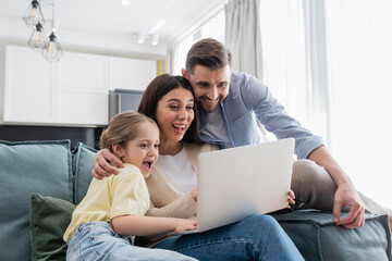 excited couple with daughter watching movie on laptop at home