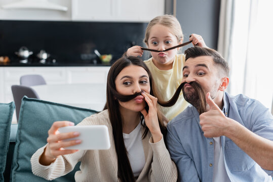 woman taking selfie with family having fun while imitating mustache with her hair