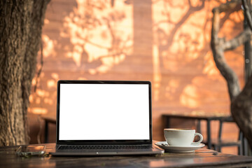 Fototapeta premium Mockup of laptop computer with empty screen with coffee cup and smartphone on table of tree branch shadow the cafe coffee shop background,White screen