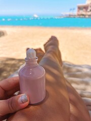 Pink bottle of oil from tanning on the legs of a girl against the background of the sea