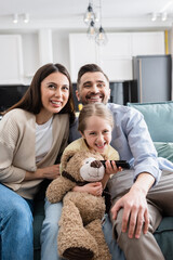 cheerful girl holding remote controller while watching tv with happy parents