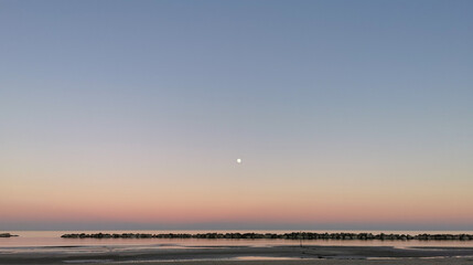 Luna sul mare in un tramonto rosa e azzurro che si riflette sulle acque del Mediterraneo