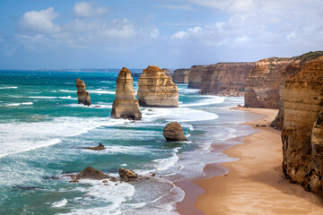 Scenic photo card on stunning views of ocean waves and steep cliffs The Twelve Apostles, Great Ocean Road, Victoria , Giant ocean waves smash against rocks near sandy beach. Sunny day.