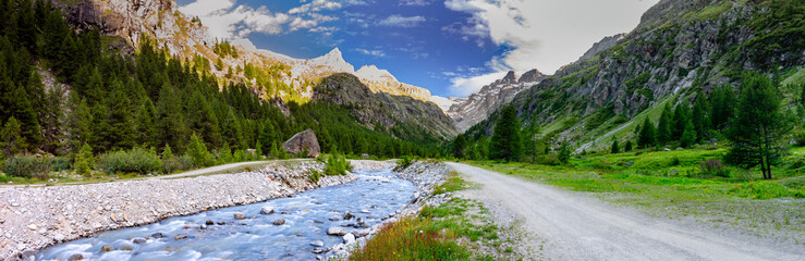 Panoramic view along the river in Valsavarenche, at dusk. Gran Paradiso National Park. View of the river, the mountains, the peaks, the meadows and the woods. Aosta Valley, Italy