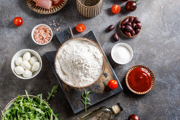 Fototapeta na wymiar Ingredients for making Italian pizza: tomato paste, mozzarella, parma ham, arugula, olives, cherry tomatoes. Ingredients for cooking 