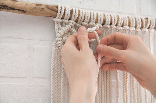 woman knits weaving macrame pinned on a wooden stick