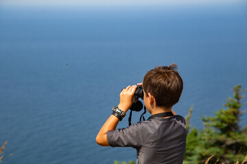 A boy looking at the beautiful ocean of Cape Breton in Nova Scotia through binoculars