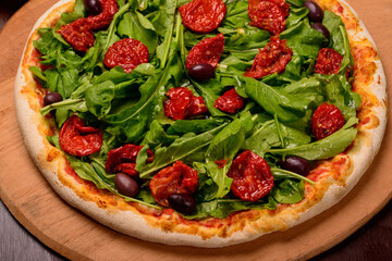 Arugula and sun dried tomato pizza on wooden board and vegetables in the background.