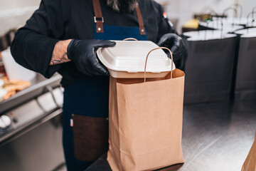 The chef prepares food in the restaurant and packs it.  Food in disposable dishes and bag of kraft paper ready for delivery.