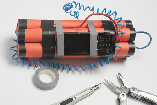 a bomb, a wire tool and an old mobile phone are being assembled on a white table as a timer before the explosion. security and counter terrorism concept