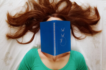 young woman with a book covering her face. Girl with loose hair and face covered by green book. Top...