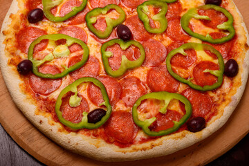 Pepperoni pizza with green peppers on wooden board and vegetables in the background.