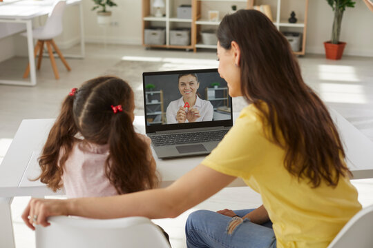 Back View Happy School Child Together With Mom Sitting At Desk Table, Looking At Laptop, Learning Letters In Online Class, Watching Teacher's Educational Kids Video In Covid19 Corona Virus Quarantine