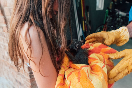 Man wearing leather gloves hands girl a raccoon in a towel. 