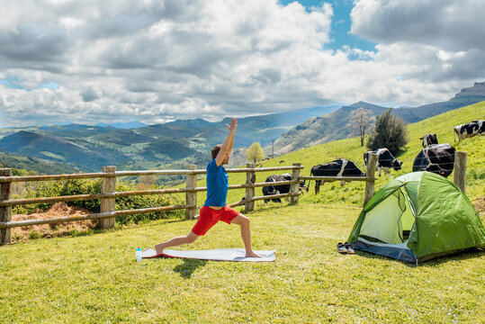Healthy man doing yoga on meadow with tent