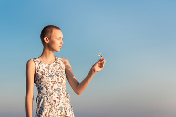 girl teenager in a dress with a short haircut looking at a flower in her hand against the...