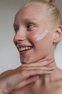 Freckled model with white clay mask on her face smiling