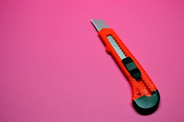 Red cutter knife on red background, sharp knife stationery
