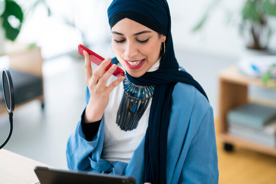 Positive Arab woman recording voice message in studio