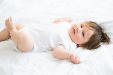 healthy 6 month baby boy smiling and lying on a white bedding at home. 