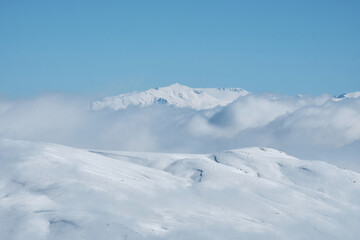Obraz premium Snow covered mountain slope with clouds and bright blue sky. Winter mountain landscape