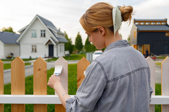 Young woman applying paint on fence in suburb