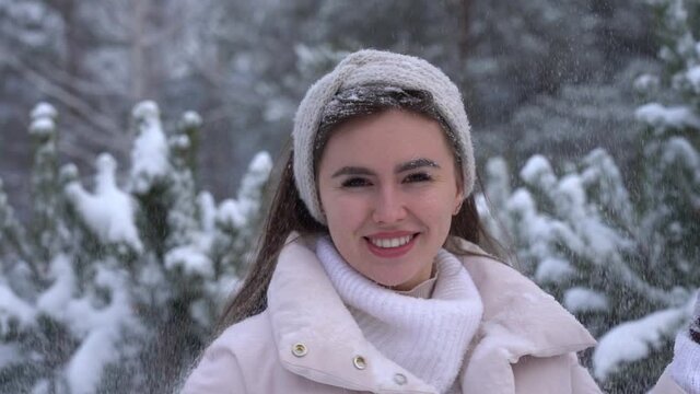 Young attractive woman throws snow and smiles in winter in the park