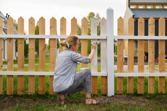 Woman sitting on haunches and painting fence
