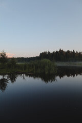 Fototapeta na wymiar summer evening twilight view on picturesque plain lake surface with reflections of sky and trees