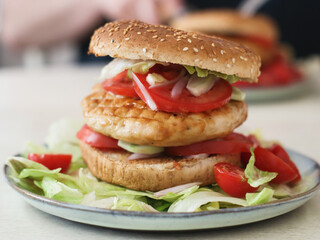 A healthy grilled chicken breast high protein and fiber hamburger with whole wheat bun and fresh green vegetables in a plate such as iceberg, cucumbers and cherry tomatoes. 