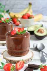 A cup of chilled healthy and non dairy, vegan avocado-banana-chocolate mousse topped with strawberries, an alternate dessert contain natural sweetener, for diet people. Paleo, ketogenic diet concept 