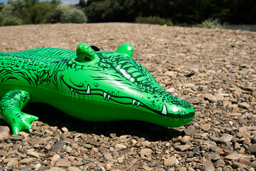 Inflatable toy green crocodile on a rocky beach