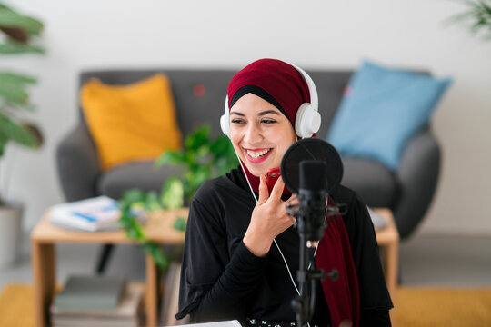 Cheerful Arab woman recording voice message on smartphone