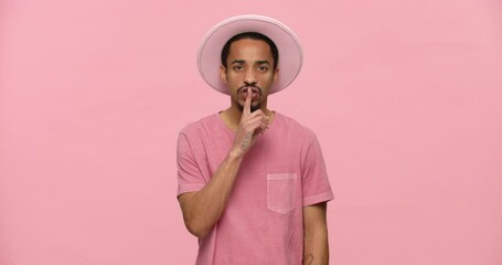 Young serious black man in pink hat showing silence gesture isolated over pink background