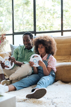 Dad and her daughter playing video games with a steering wheel at home