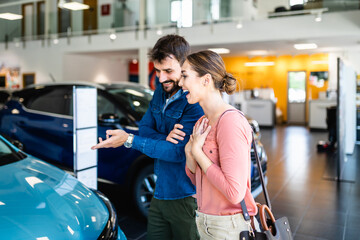 Beautiful young couple at car showroom choosing a new car to buy.