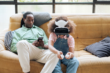 Child using virtual reality headset close to her father 
