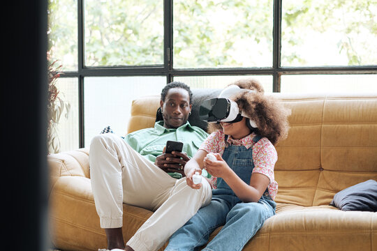 Child using virtual reality headset close to her father 