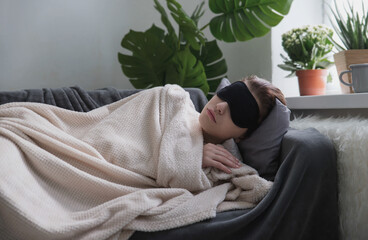 Young attractive girl in the sleeping black eye mask sleeps or naps on the couch in the room. Day...
