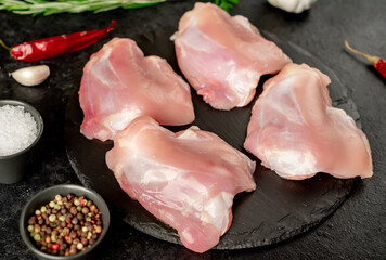 raw skinless chicken thighs with spices and herbs on a stone background