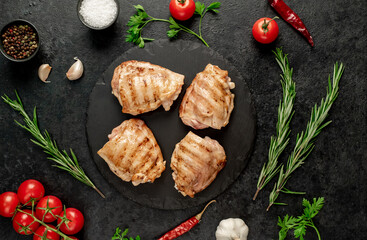 grilled skinless chicken thighs with spices and herbs on a stone background
