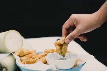 Hand picked fried calabash and dipped in seafood sauce on a black background