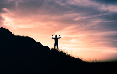Goal setting! Strong determined man on a mountain top flexing his arms up to the sky. 