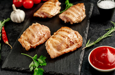 grilled skinless chicken thighs with spices and herbs on a stone background