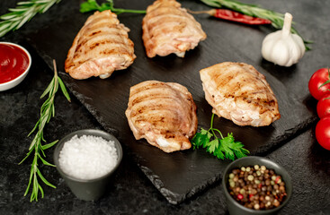 grilled skinless chicken thighs with spices and herbs on a stone background
