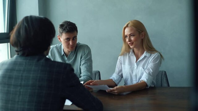 Tracking shot of positive young woman and man headhunters checking male candidate resume, asking questions during job interview with male job seeker. Shooting in slow motion.