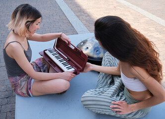 Two women opening a melodica blow organ case at street.