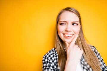 Naklejka premium Cheerful cute girl in a plaid shirt and a T-shirt thoughtfully touches her chin with her hand while thinking about something