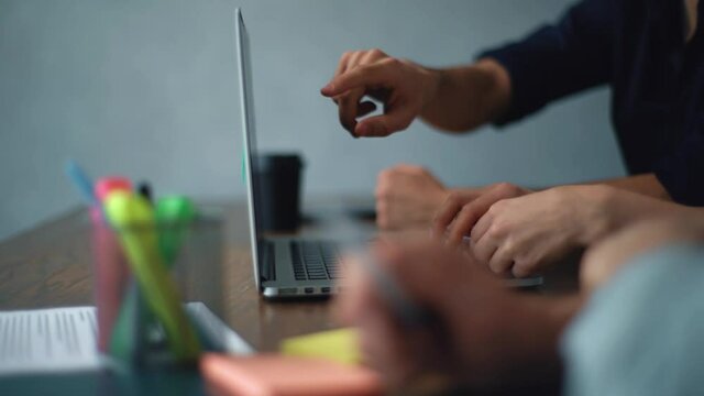 Tracking shot of unrecognizable young male and female coworkers discussing project and using laptop, gesturing and pointing at screen. Close-up of three businesspeople working at office desk together.