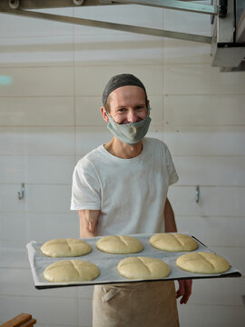 Charming portrait of a baker in the workshop  holding a bun tray.
